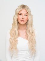 Woman with long wavy blonde hair wearing white top showcasing Sample Swatch - Bondi Root Stretch 